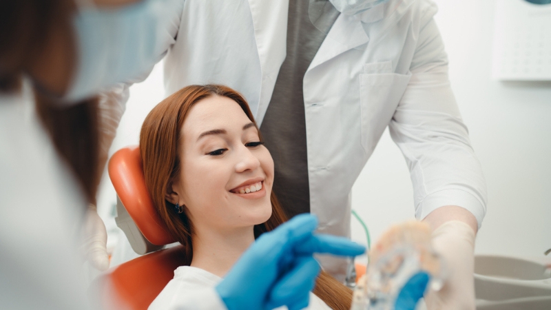 A dentist shows a smiling patient a dental model, explaining how the bridge is designed to create a natural, imperceptible gum line. 